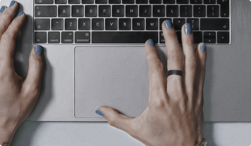 Mãos digitando em um notebook sobre uma mesa, com foco no teclado e no trackpad